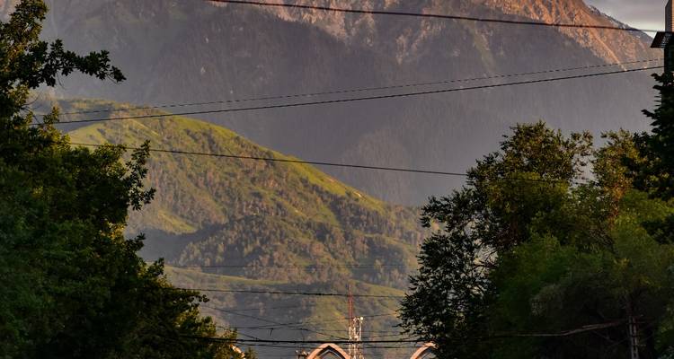 Vue urbaine de la rue regardant vers des collines verdoyantes et un arrière-plan montagneux avec des lignes électriques traversant le cadre au crépuscule.