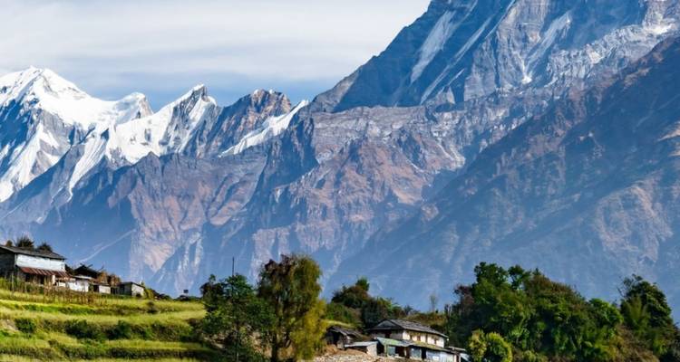 Eine Ansammlung von Terrassenfeldern und kleinen Häusern liegt unterhalb der hoch aufragenden schneebedeckten Himalaya-Klippen.