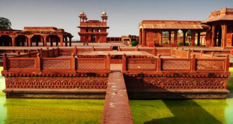 Pabellones de arenisca rojiza y estanque ornamental en Fatehpur Sikri iluminados por la luz de la tarde.