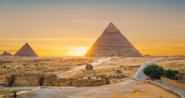 Sunset over the Pyramids of Giza with the Sphinx in foreground and orange sky behind.