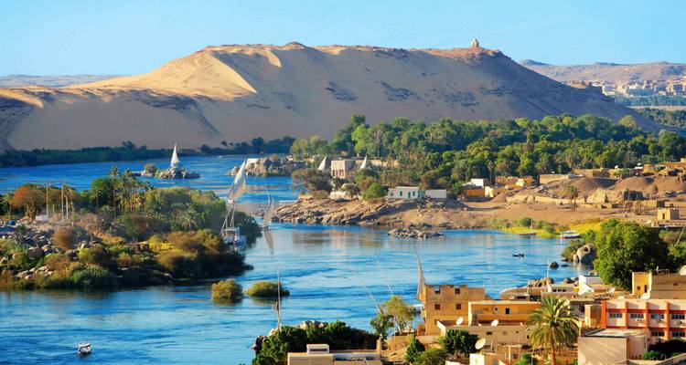 Lush Nile river curves past sandy dunes and green islands with small villages on the banks.