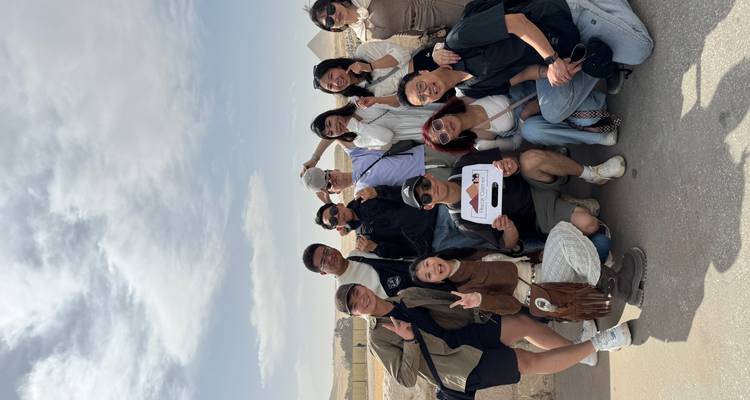 A cheerful tour group posing with a sign in front of the Pyramids of Giza.