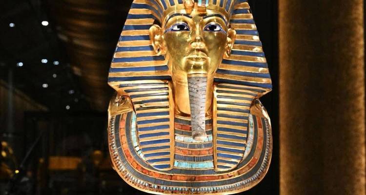 The gleaming golden funerary mask of Tutankhamun displayed under soft museum lighting.