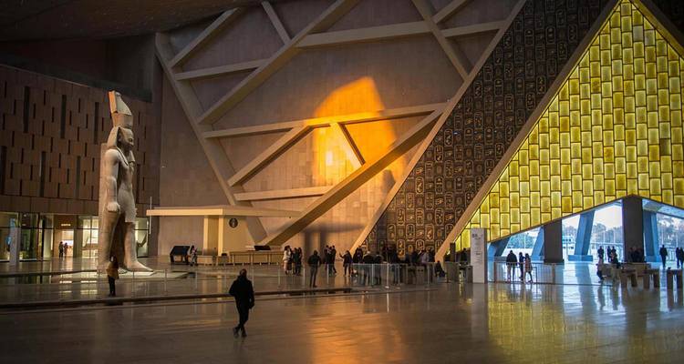 Vast modern hall of the Grand Egyptian Museum with colossal statue and patterned skylight.