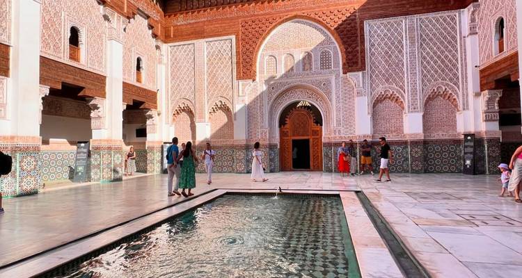 Los visitantes exploran un patio con una piscina reflectante estrecha y azulejos intrincados en una madraza marroquí.