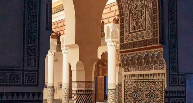 Pasillo arqueado tenuemente iluminado decorado con intrincados azulejos marroquíes y yeso tallado.