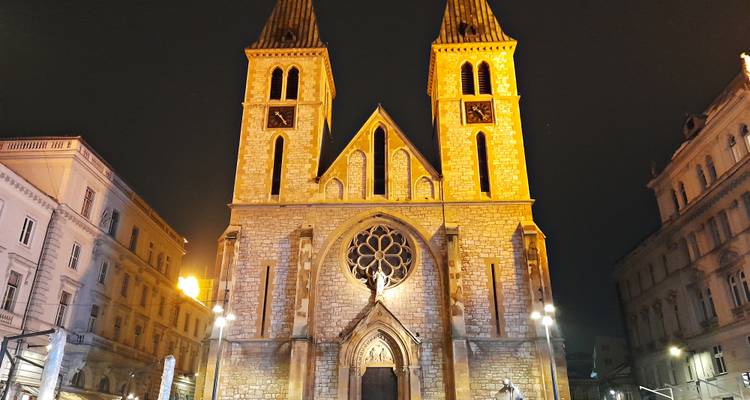 Die zweittürmige Kathedrale des Heiligen Herzens ist warm beleuchtet gegen den dunklen Nachthimmel in Sarajevos Altstadt.