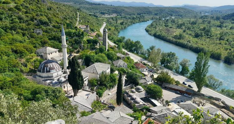 Histórico pueblo bosnio con mezquita y río visto desde arriba en medio de un verde paisaje montañoso