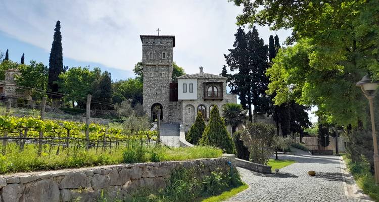 Complejo monástico de piedra rodeado de viñedos y cipreses altos a lo largo de un camino empedrado.