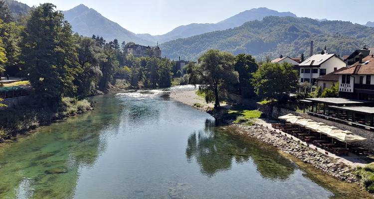 A wide river reflects surrounding forest and mountain peaks under crisp morning light.