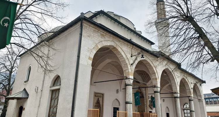 A historic white-stone mosque with arched portico stands beneath leafless trees.