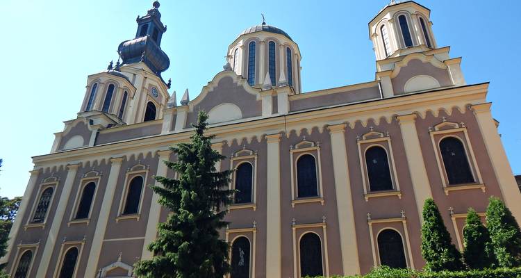 An elegant orthodox cathedral with twin towers rises against a clear sky, framed by greenery.