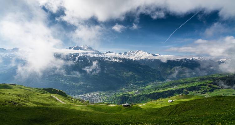 Alpine valley with scattered clouds revealing snow-capped peaks and lush green hillsides.