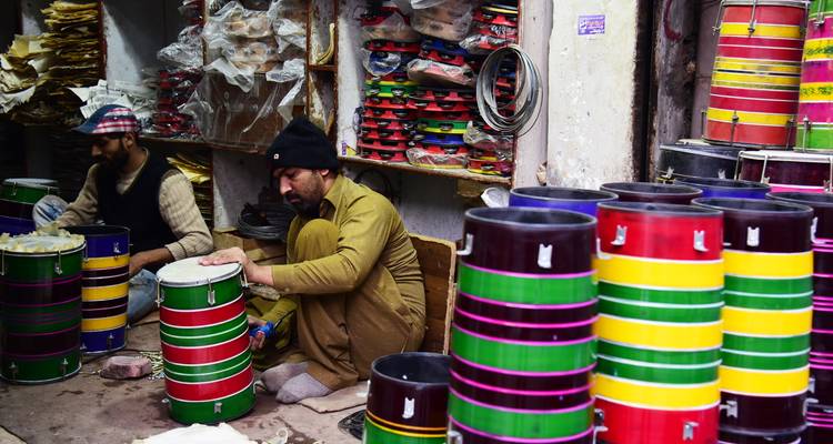 Des artisans fabriquent des tambours colorés à la main dans un atelier encombré rempli de peinture et d'outils.