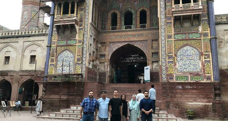 Cinq visiteurs posent sur les marches de pierre devant l'entrée ornée et recouverte de carreaux de la mosquée Wazir Khan.