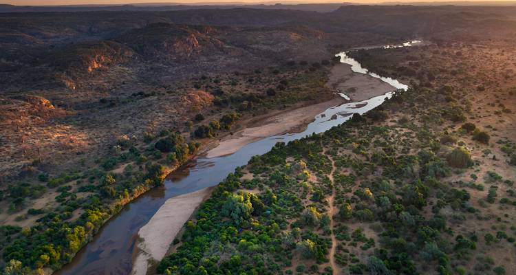 Drone shot of a winding river cutting through rugged hills at golden hour