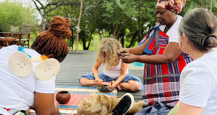 Small gathering on a wooden deck as a local woman demonstrates traditional craftwork to visitors seated around her.