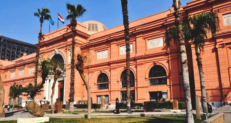 Pink-hued Egyptian Museum façade flanked by tall palm trees under clear blue sky.