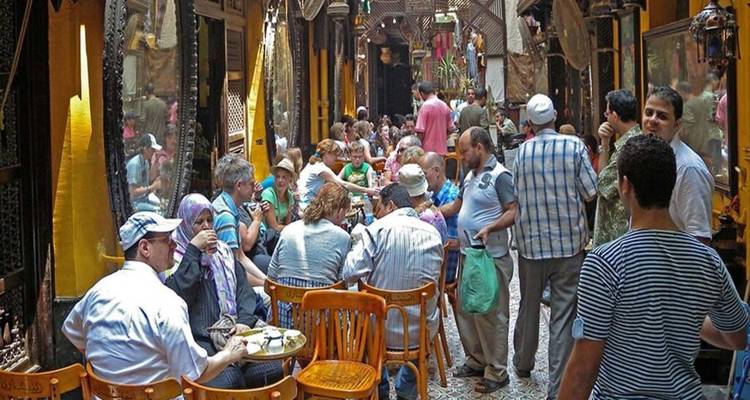 Bustling alley café where locals and tourists sit at wooden tables enjoying drinks.