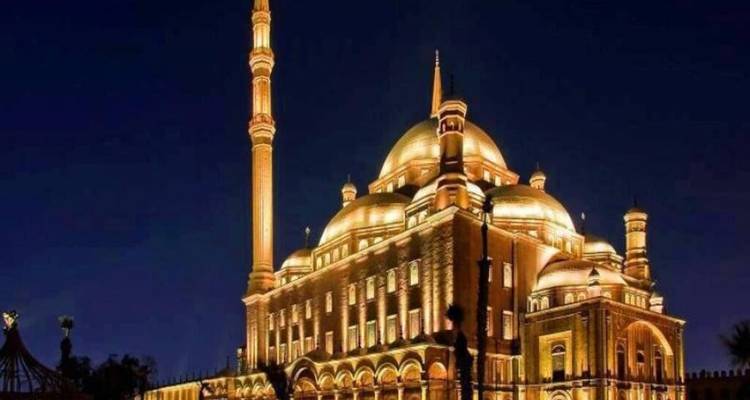 Golden-lit mosque with towering minaret glowing against a deep night sky.