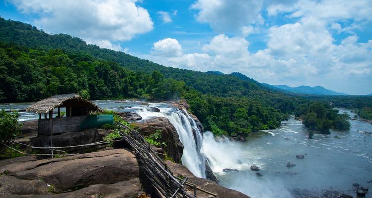 Powerful waterfall plunging over a rocky ledge surrounded by dense tropical forest with a rustic viewpoint hut.