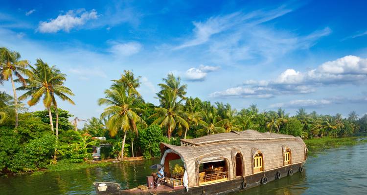 Traditional Kerala houseboat drifting along lush green backwaters under a vivid blue sky.