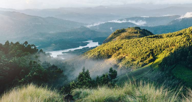 High vantage view over misty mountains, a winding lake, and verdant forested slopes at dawn.