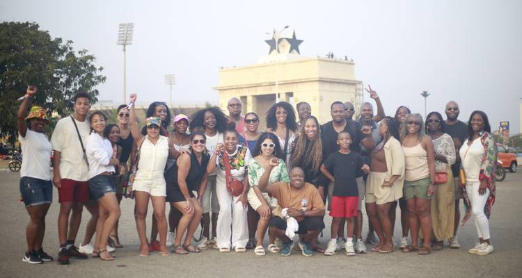 Large tour group posing energetically in front of Independence Arch and Black Star Square