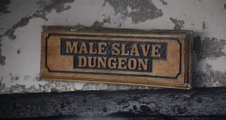 Wooden plaque reading 'Male Slave Dungeon' mounted on an aged, weathered wall