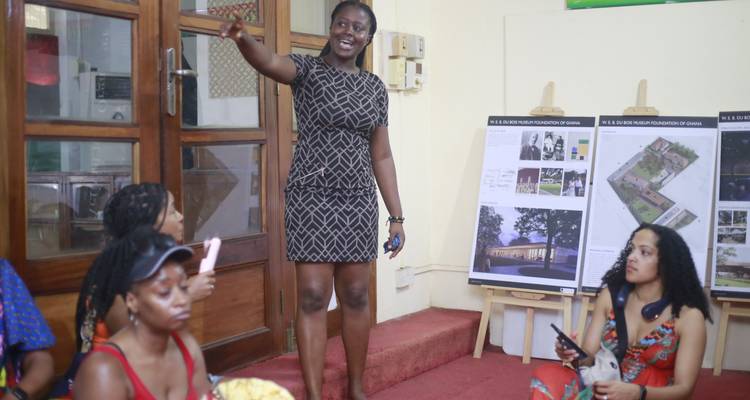 Local guide presenting information boards to seated visitors in an indoor classroom setting