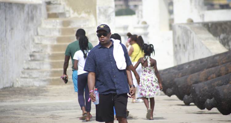Visitors walking along ramparts with old cannons at a coastal slave fort