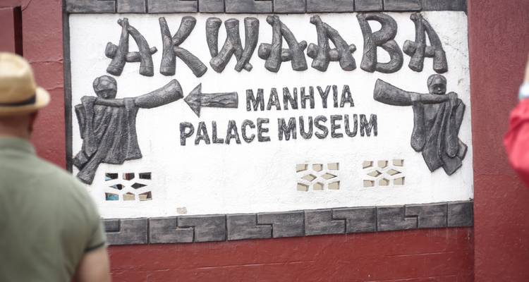 Welcome sign for Manhyia Palace Museum with tourists walking past.