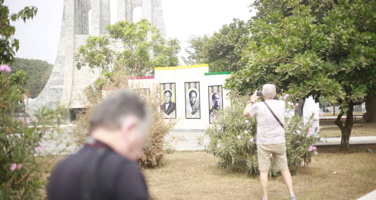 Visitors taking photos near murals of Ghanaian leaders at an outdoor memorial garden.