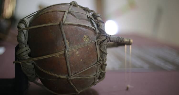 Close-up of a traditional West African talking drum on display against a purple wall.