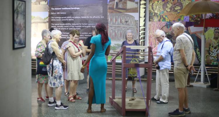 Museum guide in turquoise dress explaining an exhibit to a group of attentive tourists.