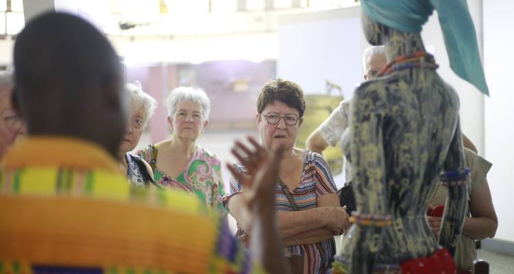 Guide gestures toward a life-size statue while mature visitors listen during a museum tour.