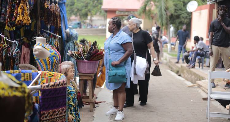 Les voyageurs parcourant des tissus aux motifs éclatants et des objets artisanaux à un étal de marché en plein air