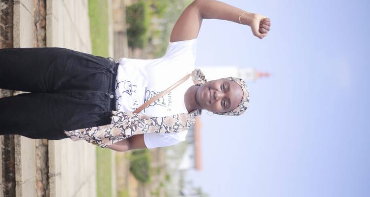 Young woman raises her fist in front of Accra’s red-and-white Jamestown Lighthouse.