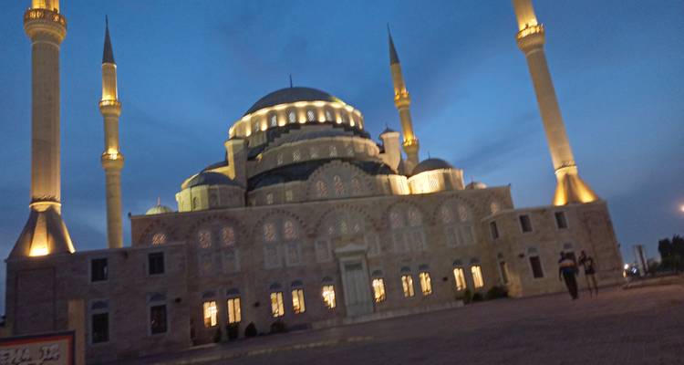 Nighttime photo of Accra’s illuminated National Mosque, slightly blurred against a blue twilight sky.