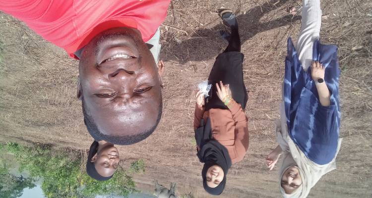 Selfie of travellers in a dry field with a distant elephant wandering in the background.