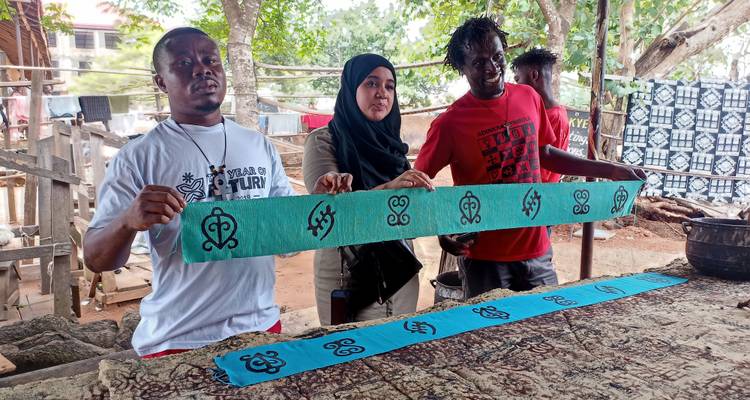 Visitors proudly display hand-printed fabric strips at an outdoor craft workshop.