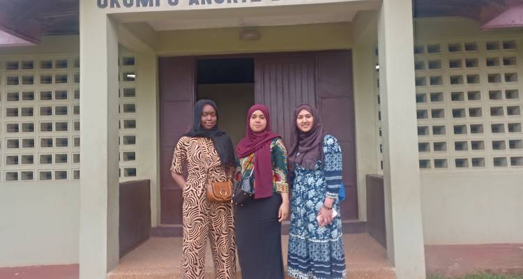 Three women stand outside a modest museum entrance with concrete steps.