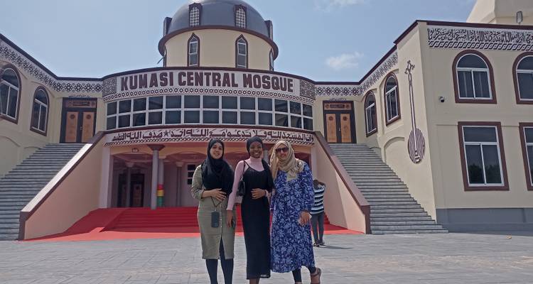 Travellers pose on the red-carpeted steps of Kumasi Central Mosque under clear skies.