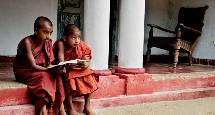 Deux jeunes moines bouddhistes sont assis sur les marches du monastère et étudient un livre ensemble.
