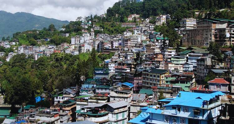 Dense hillside cityscape of Gangtok featuring colorful rooftops nestled among green forested hills.