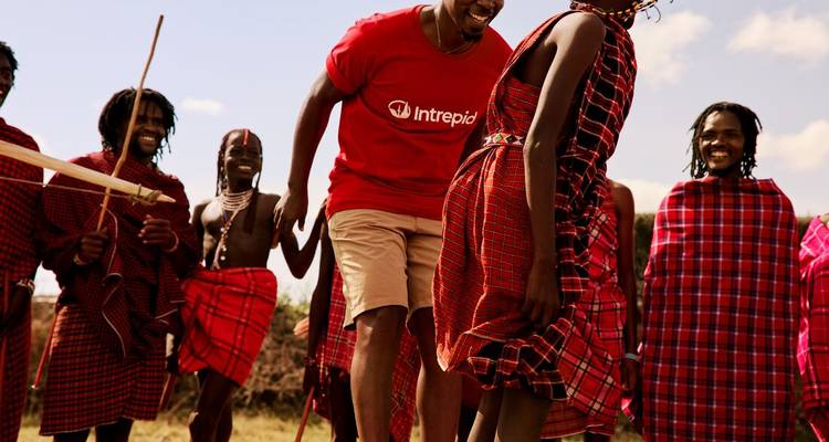 Maasai villagers and a visitor laugh and dance together wearing bright red shukas.