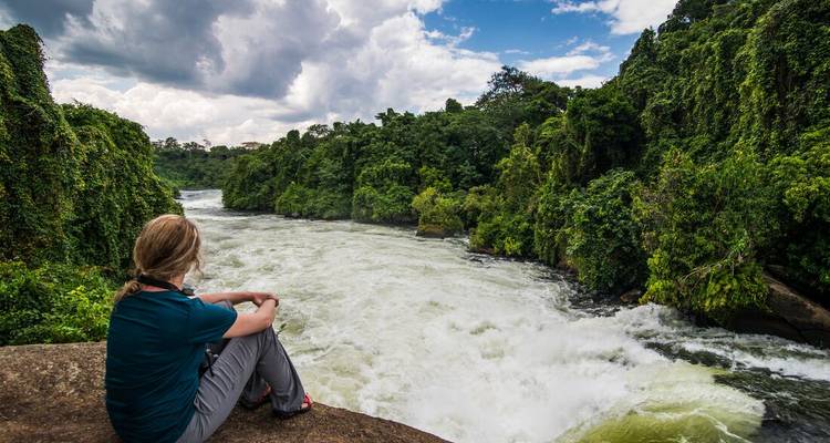 Traveller sits on a rock overlooking powerful jungle rapids winding through lush canyon walls.