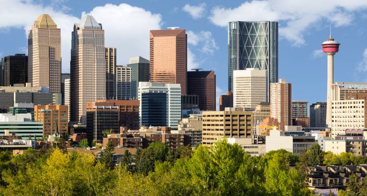 Clear daytime shot of Calgary’s modern skyline featuring the Calgary Tower rising above green treetops.