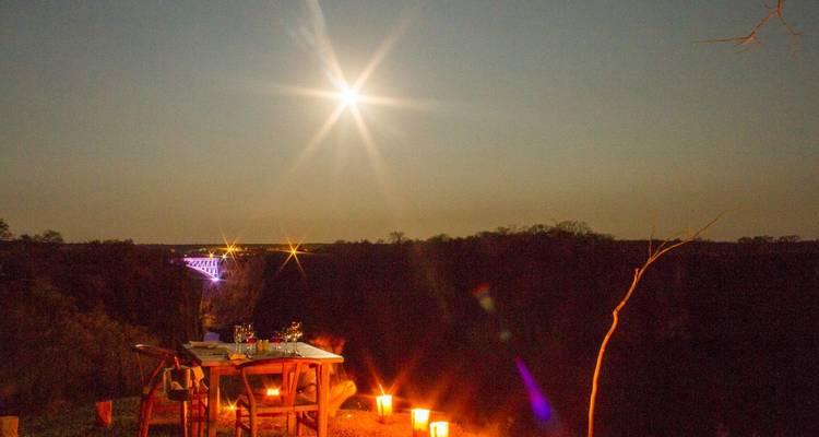 Une table de diner romantique en plein air éclairée par des bougies sous une lune brillante près d'une gorge fluviale