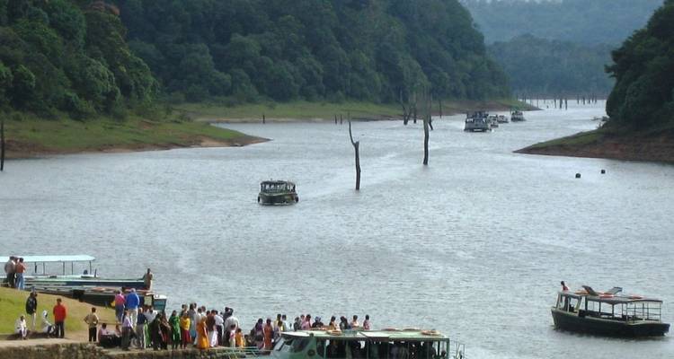 Crowds board sightseeing boats on the calm waters of Periyar Lake bordered by dense forest.